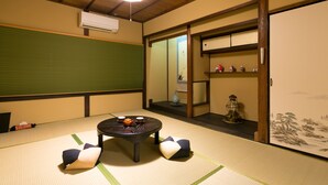 A tatami mat room with a low table, cushions, a hanging light, and a sliding door with a view.
