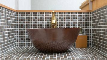 A bathroom with a large, round, brown ceramic sink with a gold faucet, set against a tiled wall with a grid pattern.