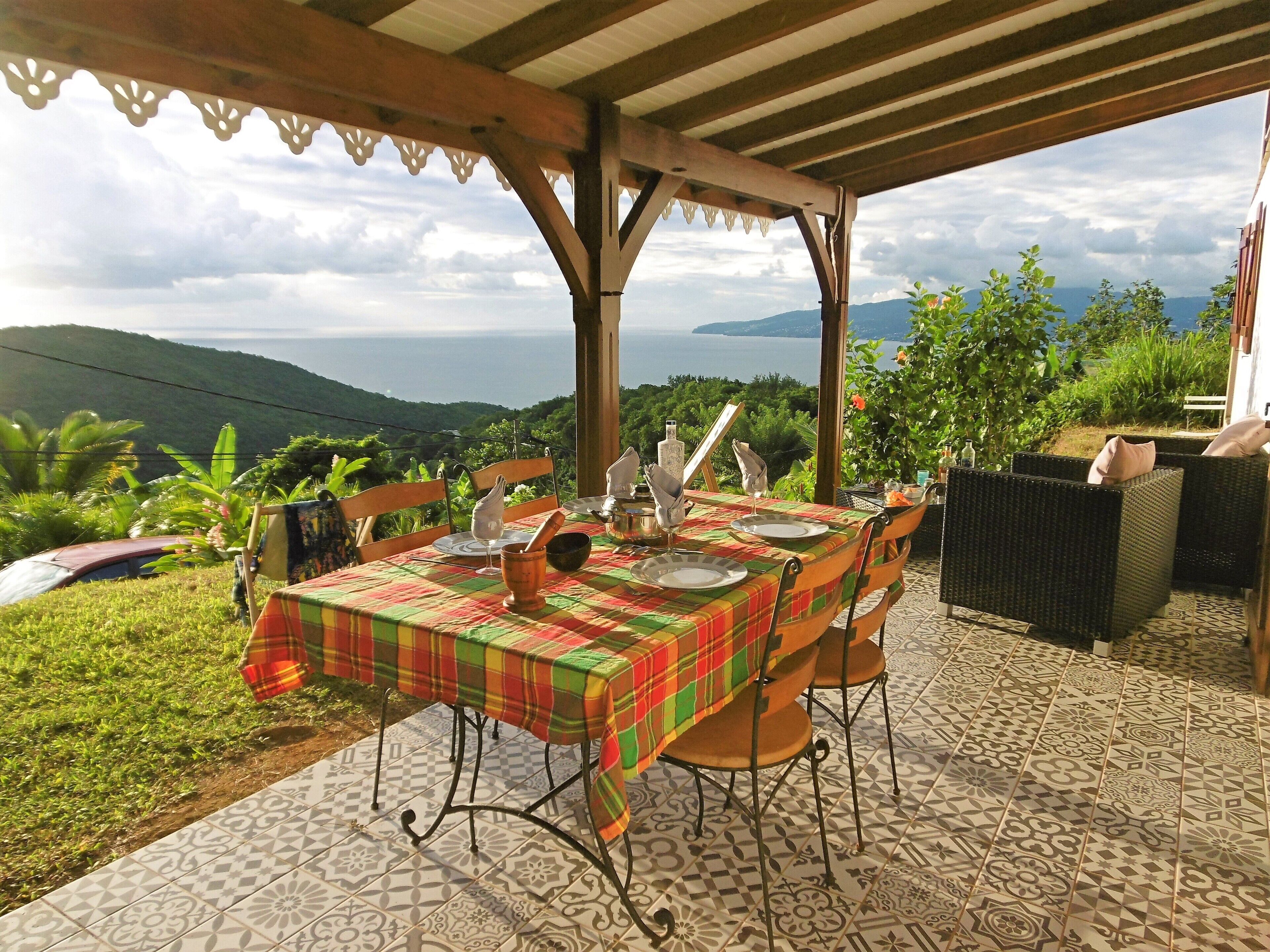 An outdoor dining area with a view of the sea and hills, covered patio, and tiled flooring.