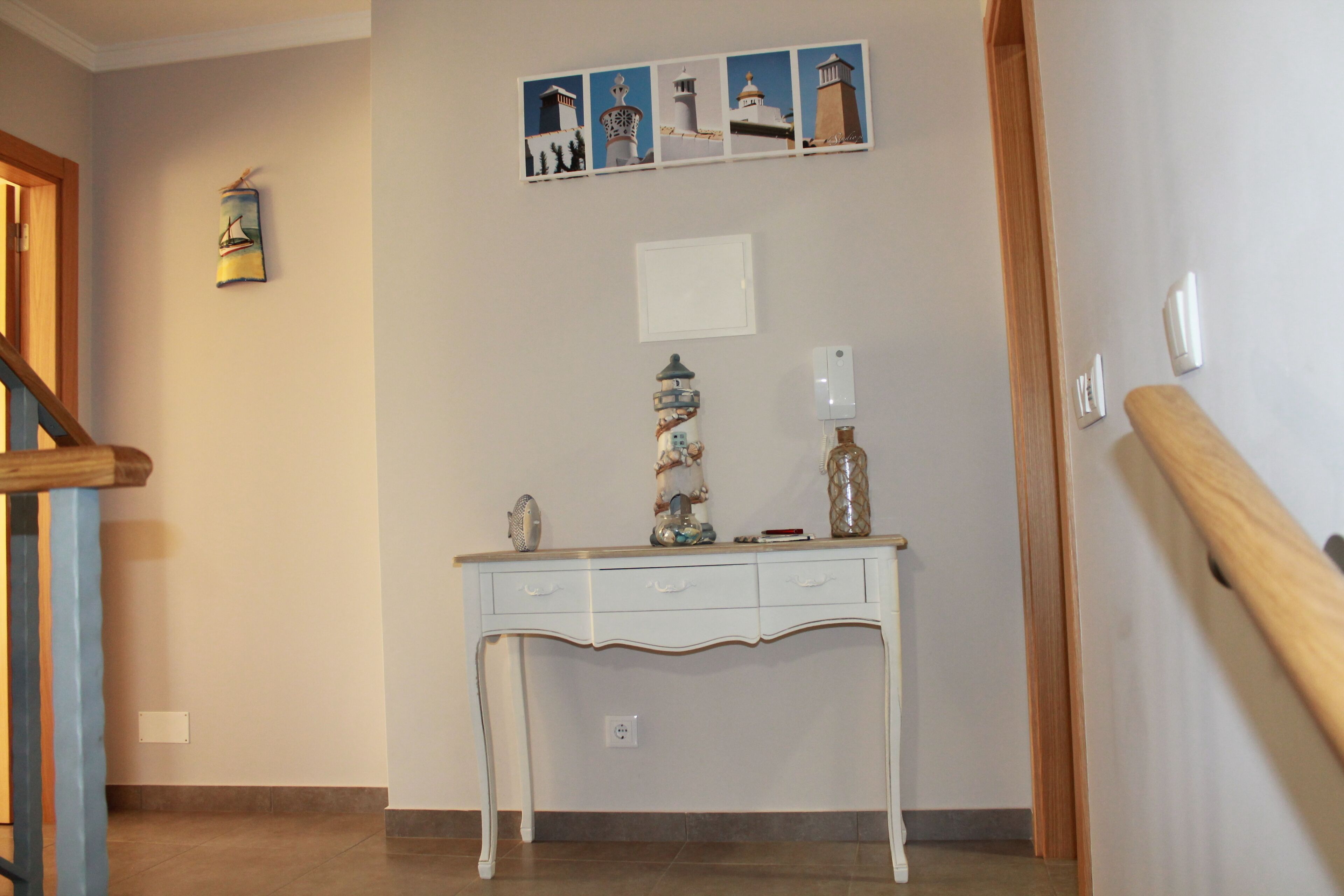 A hallway with a white console table, a small shelf with decorative items, and a series of framed pictures on the wall.