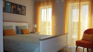 A bedroom with a bed, a chair, a nightstand, and a window with curtains. - Mar i Terra, the home of your vacation! (olhao)