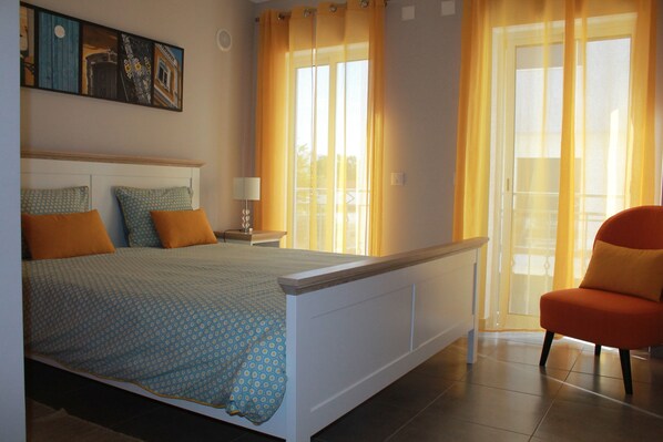 A bedroom with a bed, a chair, a nightstand, and a window with curtains. - Mar i Terra, the home of your vacation! (olhao)