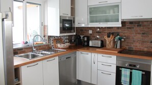 A modern kitchen with white cabinets, a brick backsplash, stainless steel appliances, and a window with a view. - Mar i Terra, the home of your vacation! (olhao)