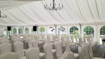 A tented event space with rows of white chairs and arched windows.