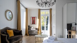 A hotel room with a bed, a sofa, a small round table, a desk, and a large window with curtains.