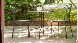 An outdoor seating area with a table and two chairs, surrounded by trees.