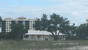 Ein Strand mit einem Gebäude, das eine überdachte Veranda und einen Baum im Vordergrund hat.