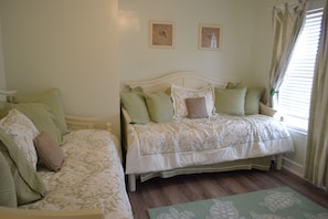 A bedroom with two beds, each with green and white bedding, a wooden floor, and two framed pictures on the wall.
