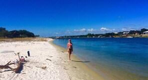A beach with clear blue water, a sandy shore, and a pier in the background.