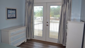 Ein Zimmer mit weißem Schminktisch, einem gerahmten Bild an der Wand und einer Tür, die auf einen Außenbereich mit einer Holzterrasse führt.
