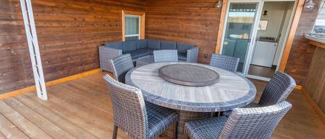 A wooden deck with a round table and wicker chairs, a built-in bench, and a sliding glass door leading to an interior space.