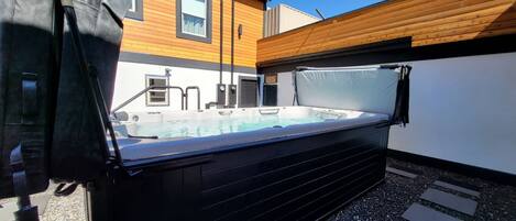 Una vasca idromassaggio in un giardino sul retro, con un pontile in legno, una piccola piscina e una casa sullo sfondo.