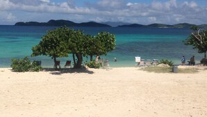 Una playa con agua turquesa cristalina, algunos árboles y un cartel que dice "Stay Off The Coral".
