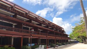 Un edificio de varios pisos con balcones, suelo arenoso y cielo despejado.