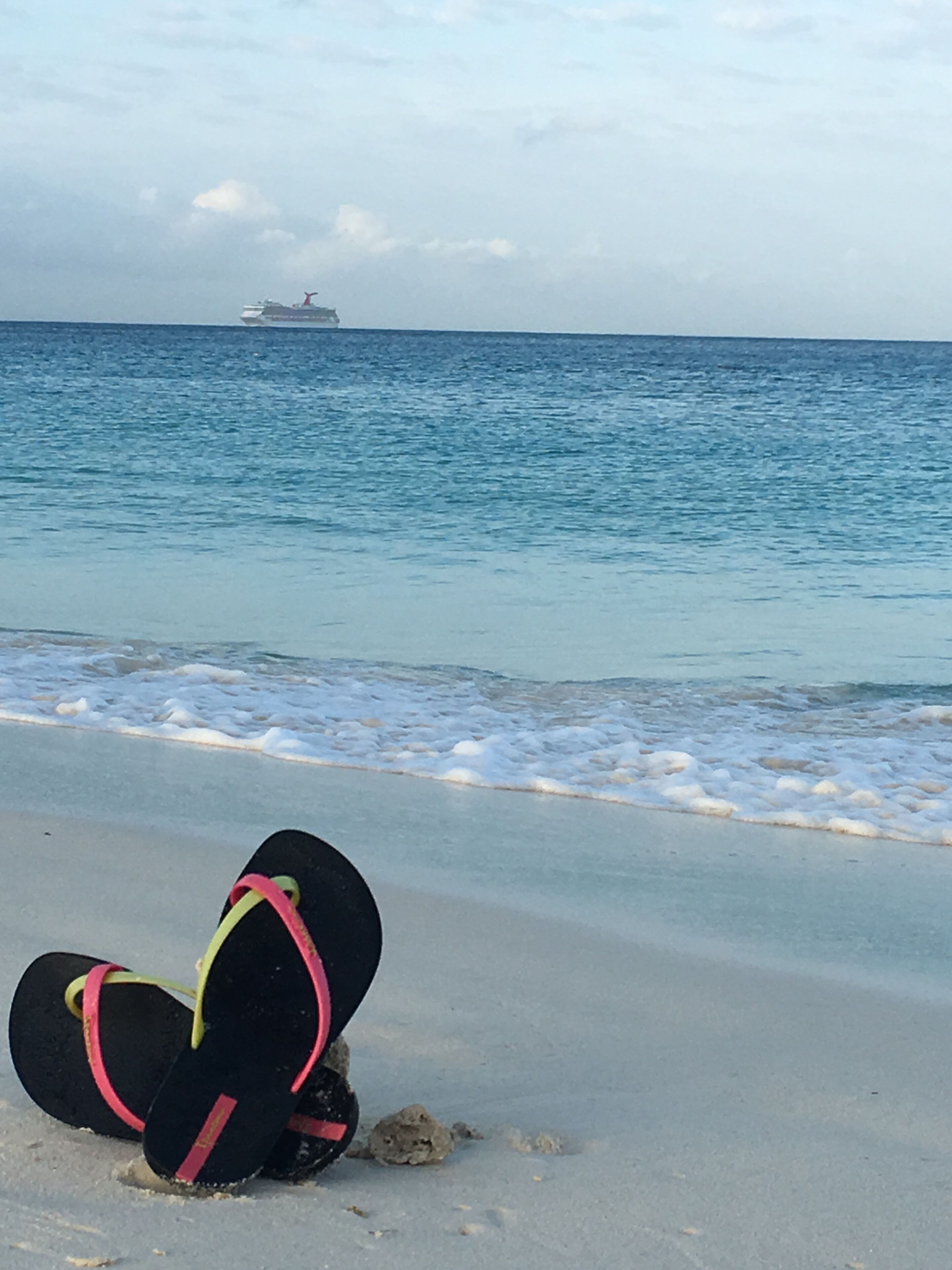 Un par de chanclas sobre una playa arenosa con un barco a lo lejos.