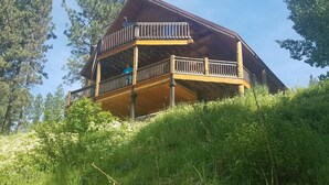 Een houten chalet met een balkon, omgeven door weelderige begroeiing en hoge bomen.