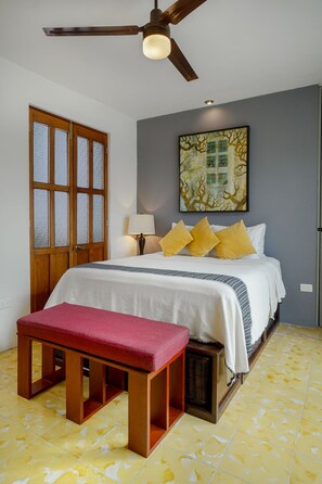 A bedroom with a bed, a bench, a ceiling fan, and a window with frosted glass.