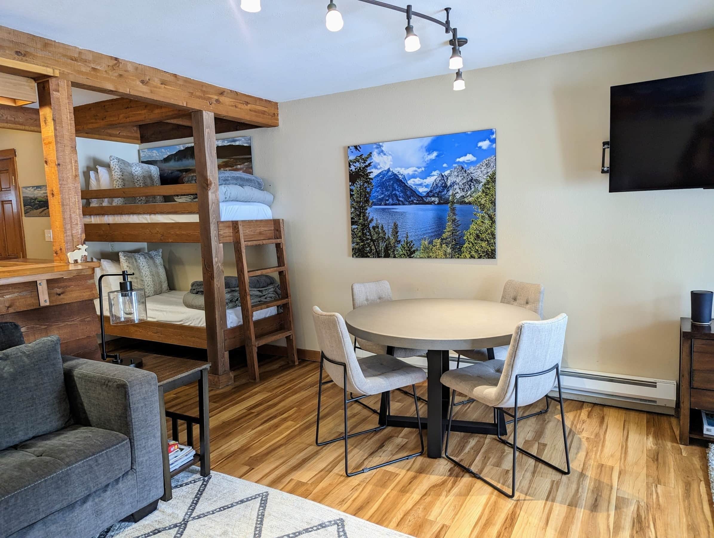A cozy room with a bunk bed, a round dining table with chairs, a sofa, and a mounted TV.