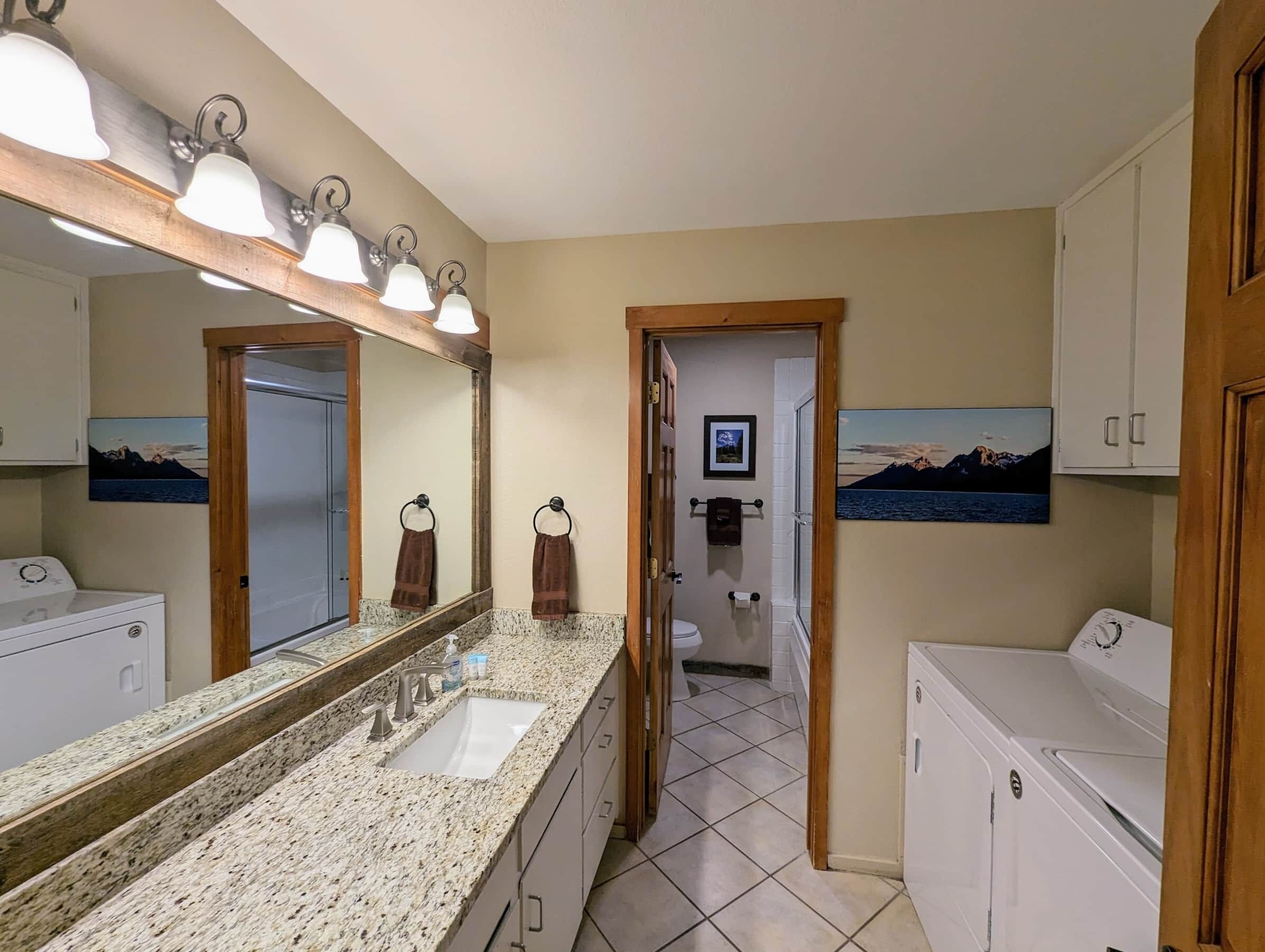 Ein Badezimmer mit zwei Waschbecken, einem großen Spiegel und einer Dusche. Handtücher hängen an der Wand, und ein Bild ist über der Toilette angebracht.