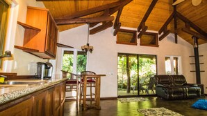 A spacious living area with a wooden ceiling, a kitchen with a granite countertop, and a sliding glass door leading to a patio. - Private Cottage In The Rain Forest TA065882726401 (Kailua-Kona)