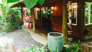 A wooden house with a porch, surrounded by lush greenery and potted plants. - Private Cottage In The Rain Forest TA065882726401 (Kailua-Kona)