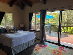 Une chambre à coucher comprenant un lit, une table de chevet, une fenêtre avec des rideaux et une vue sur une terrasse extérieure avec une table et des chaises.