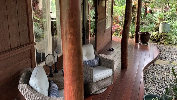 A covered porch with wicker furniture, a wooden floor, and potted plants. - Private Cottage In The Rain Forest TA065882726401 (Kailua-Kona)