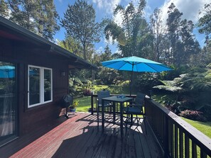 Une terrasse en bois avec une table et des chaises, un parasol bleu et un jardin agrémenté de diverses plantes et arbres.