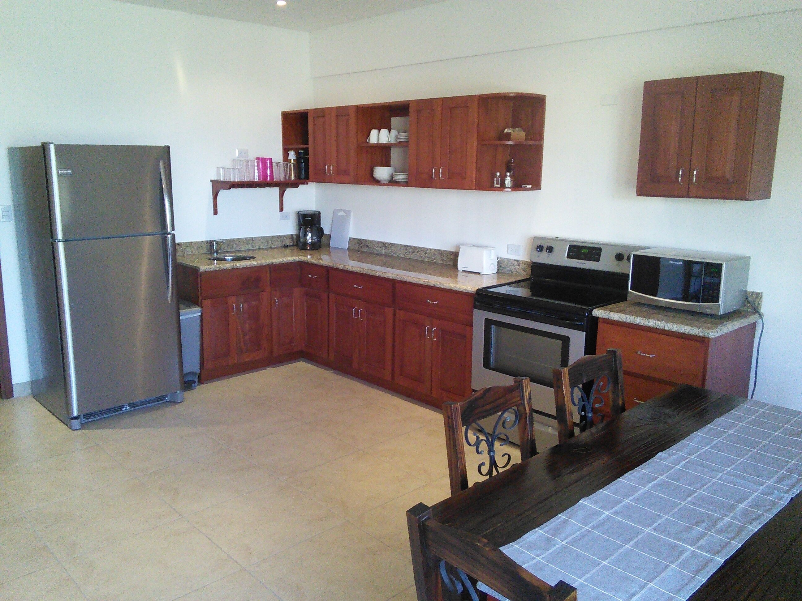 A kitchen with wooden cabinets, a stainless steel refrigerator, a microwave, and a stove.
