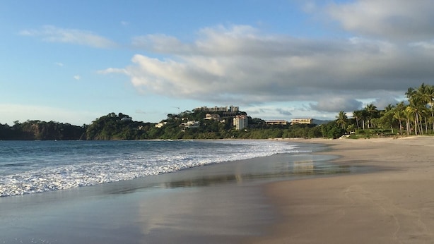 Una playa con vista despejada al océano y un complejo de edificios al fondo.