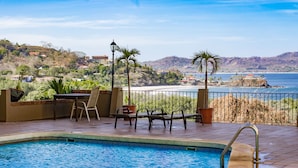 Zona de piscina con vista al océano y colinas.