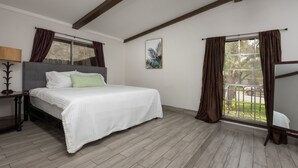 Un dormitorio con cama, mesita de noche, ventana con cortinas y vistas al exterior.