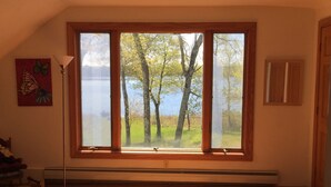 A room with a large window overlooking a lake and trees, a wooden floor, and a radiator.