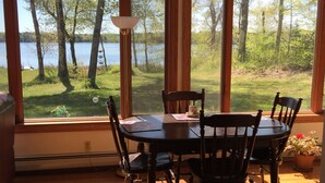A dining area with a table and chairs, large windows with a view of a lake and trees, and a lamp on the table.