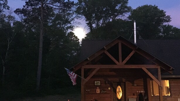 A wooden cabin with a porch, a flag, and a large circular emblem on the front.