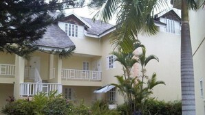 A multi-story building with balconies, surrounded by tropical plants and a palm tree. - Ocho Rios Modern Self Contained Studio with pool, cable, LED TV, fast Internet. (Ocho Rios)