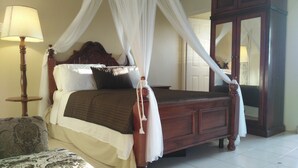 A four-poster canopy bed with a wooden headboard, white bedding, and a nightstand with a lamp. - Ocho Rios Modern Self Contained Studio with pool, cable, LED TV, fast Internet. (Ocho Rios)