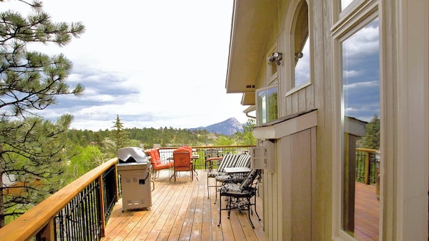 Una terraza de madera con mobiliario exterior, una parrilla y vistas a la montaña.