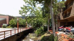 A view of a river flowing through a landscaped area with a bridge and a parking lot with cars. - Beautiful Downtown Gatlinburg Smokey mountain condo  (Gatlinburg)