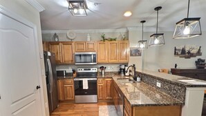 A kitchen with wooden cabinets, a granite countertop, stainless steel appliances, and pendant lighting. - Beautiful Downtown Gatlinburg Smokey mountain condo  (Gatlinburg)