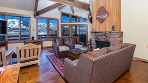 A spacious living room with a stone fireplace, wooden beams, and large windows offering mountain views. - New Remodeled interior plus outside updated in Upper DV walk to Silver Lake (DEER VALLEY)
