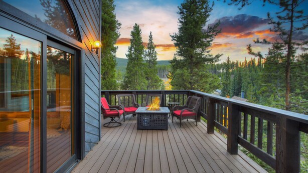 A wooden deck with outdoor seating and a fire feature, overlooking a forested landscape. - Spacious 3-Story Breck Mountain Home - Pet-Friendly, Peak 10 Views & Hot Tub (Brekenridge)