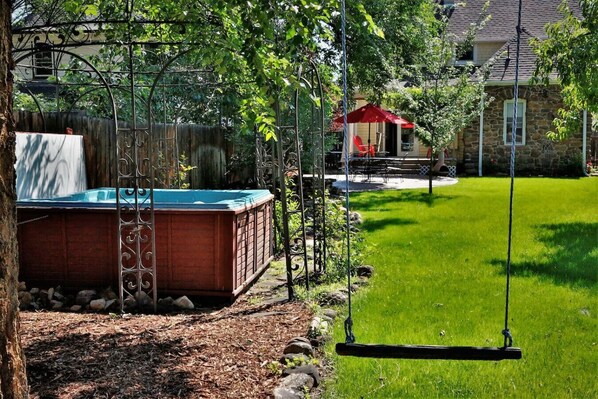 A backyard with a hot tub, a swing set, and a stone house in the background. - Old North End Victorian (Colorado Springs)