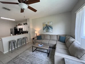 Ein modernes Wohnzimmer mit Sofa, Couchtisch und einer Küche im Hintergrund.