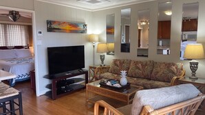 Una sala de estar con una televisión de pantalla plana, un sofá, una mesa de centro y un comedor con una silla.