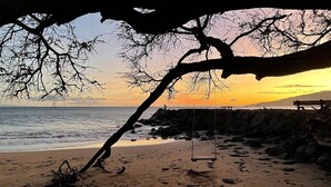 Una playa con un columpio, costa rocosa y un atardecer.