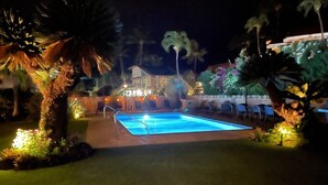 Piscina rodeada de palmeras y un edificio al fondo.