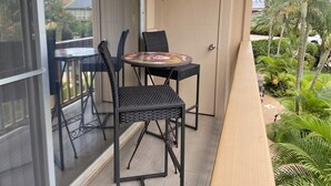Un espacio al aire libre cubierto con mesa y dos sillas, una puerta y vista a un jardín con palmeras.