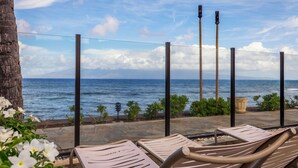 Eine Strandlounge mit Liegestühlen, die zum Meer ausgerichtet sind, einem Steinweg und Blick auf See und Himmel.