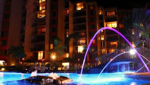 Ein Schwimmbad bei Nacht mit Wasserspielen und einem Gebäude im Hintergrund.